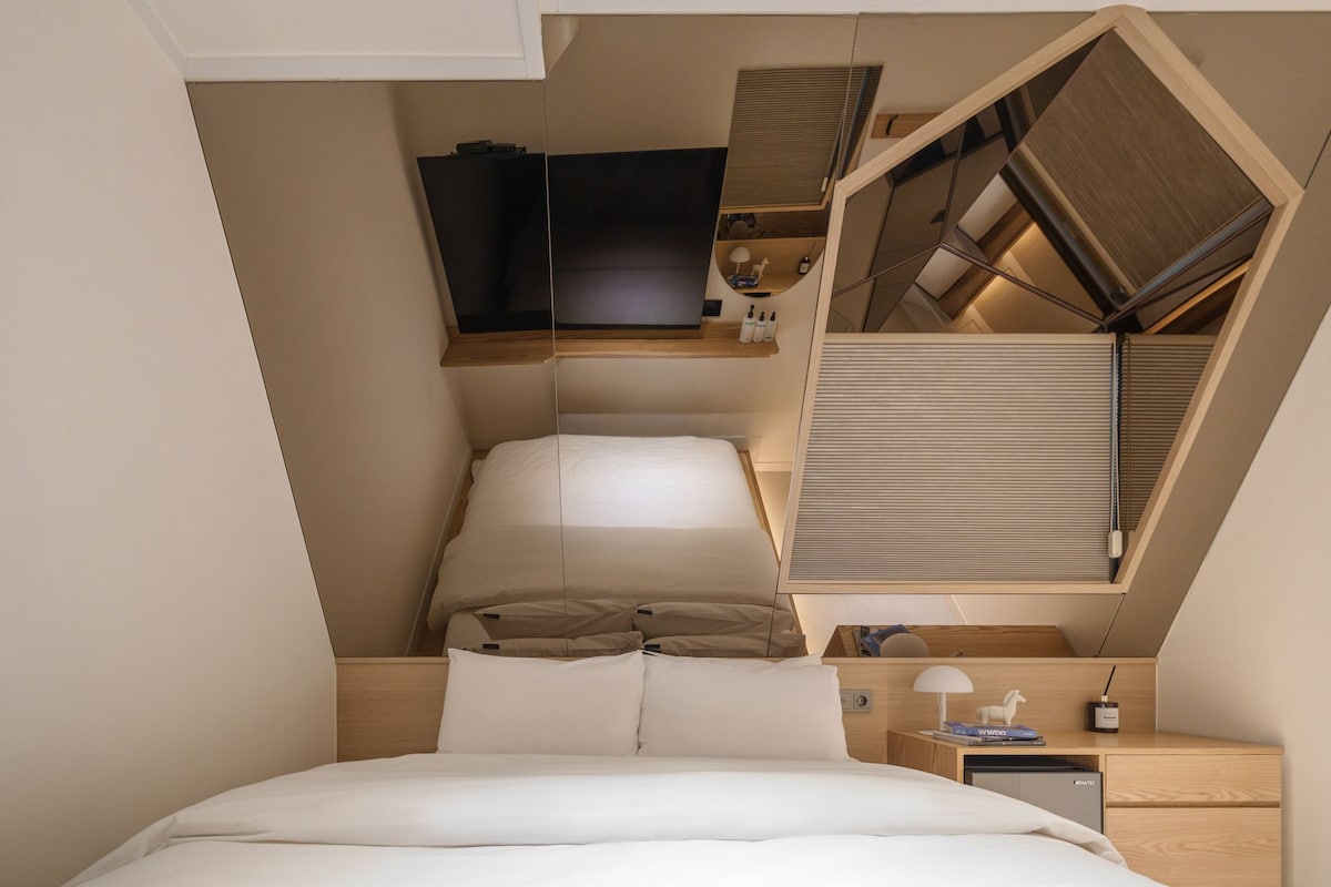 A bedroom with a bed, a nightstand, a lamp, and a TV mounted on the wall.