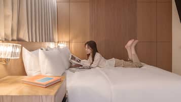 A person lying on a bed in a hotel room, reading a book.