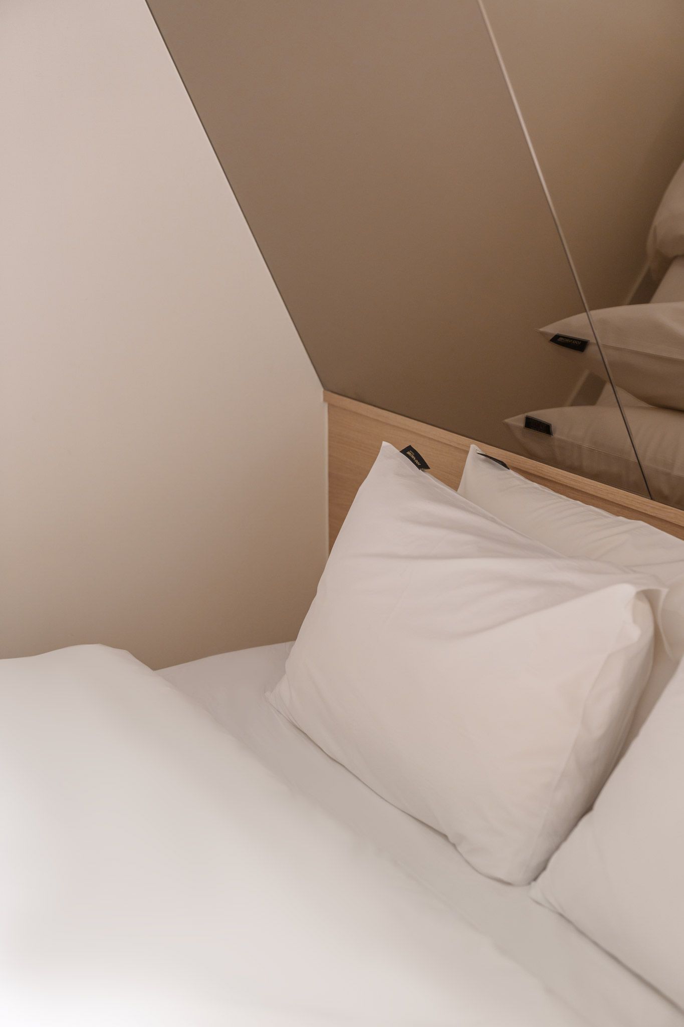 Cama bem arrumada com roupa de cama e almofadas brancas, cabeceira de madeira e um espelho refletindo parte do quarto.