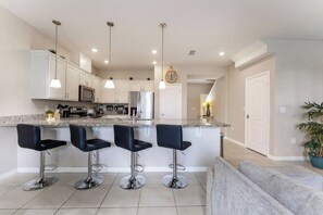 A modern kitchen with a central island, bar stools, and stainless steel appliances. - Next to Disney! 4/4 Townhome, Themed Rooms, 6 Beds (Kissimmee)