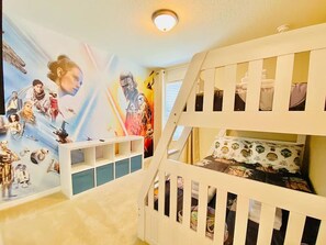 Une chambre d’enfant avec une fresque murale sur le thème de Star Wars, des lits superposés et un plafonnier blanc.