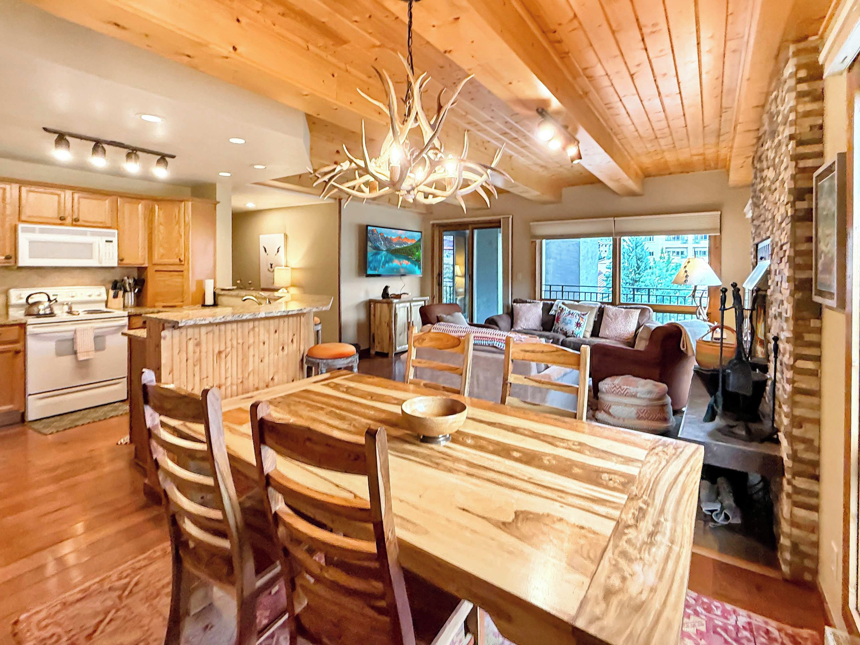 A wooden interior with a dining table, chairs, a kitchen area, and a living space with a sofa and a television.