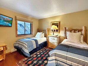 A hotel room with two beds, a window with blinds, a television, a wooden dresser, and a patterned rug. - NEW LISTING - Plaza 2 Bedroom Basecamp—Steps to Trails & Lift! (Crested Butte)