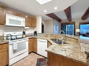 A modern kitchen with granite countertops, wooden cabinets, a built-in oven, and a stainless steel sink. - Plaza 2BR Mountain View (Crested Butte)