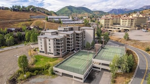 A multi-story building with a flat roof, surrounded by a parking area and tennis courts. - Plaza 2BR Mountain View (Crested Butte)