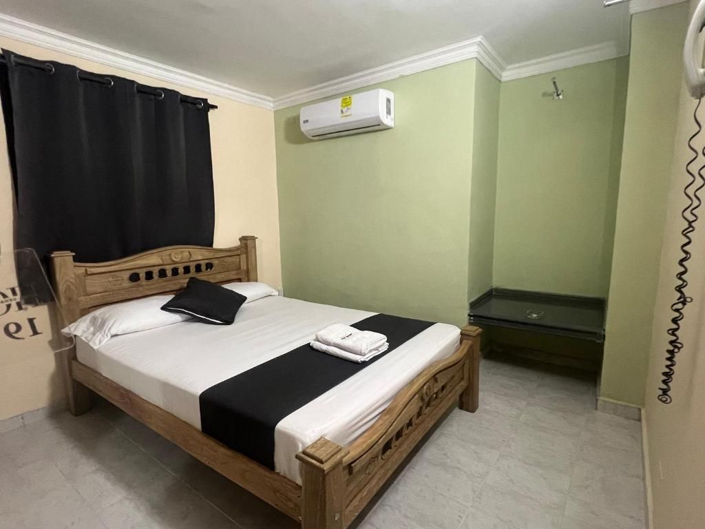 A single bed with a wooden frame, a black and white bedspread, and a black pillow. There is a white air conditioning unit mounted on the wall above the bed.