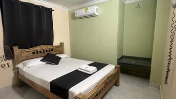 A single bed with a wooden frame, a black and white bedspread, and a black pillow. There is a white air conditioning unit mounted on the wall above the bed.