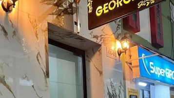 L’entrée d’un hôtel, avec une façade en marbre, une porte en verre et un panneau lumineux au néon indiquant « Super G ».