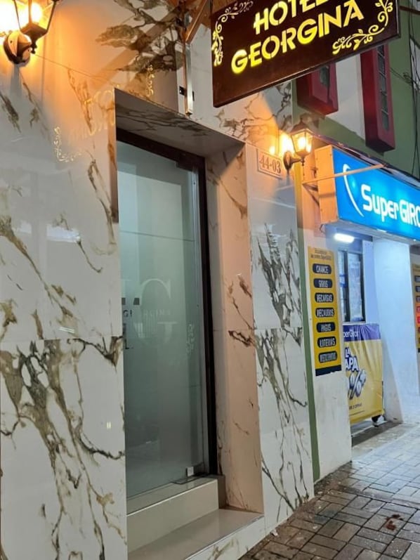 A hotel entrance with a marble facade, a glass door, and a neon sign for 'Super G'.