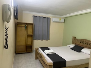A bedroom with a bed, a wardrobe, a telephone, and an air conditioning unit.