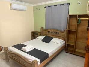 A single bed with a wooden headboard, a nightstand, a wardrobe, and an air conditioning unit on the wall.