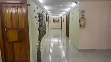 Un couloir avec une porte en bois, un extincteur et un tableau encadré accroché au mur.