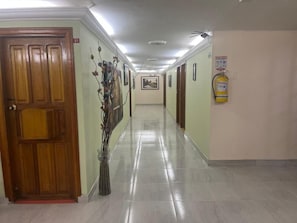 A hallway with a wooden door, a fire extinguisher, and a framed picture on the wall.