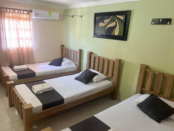 A room with two wooden beds, a painting on the wall, and an air conditioning unit.