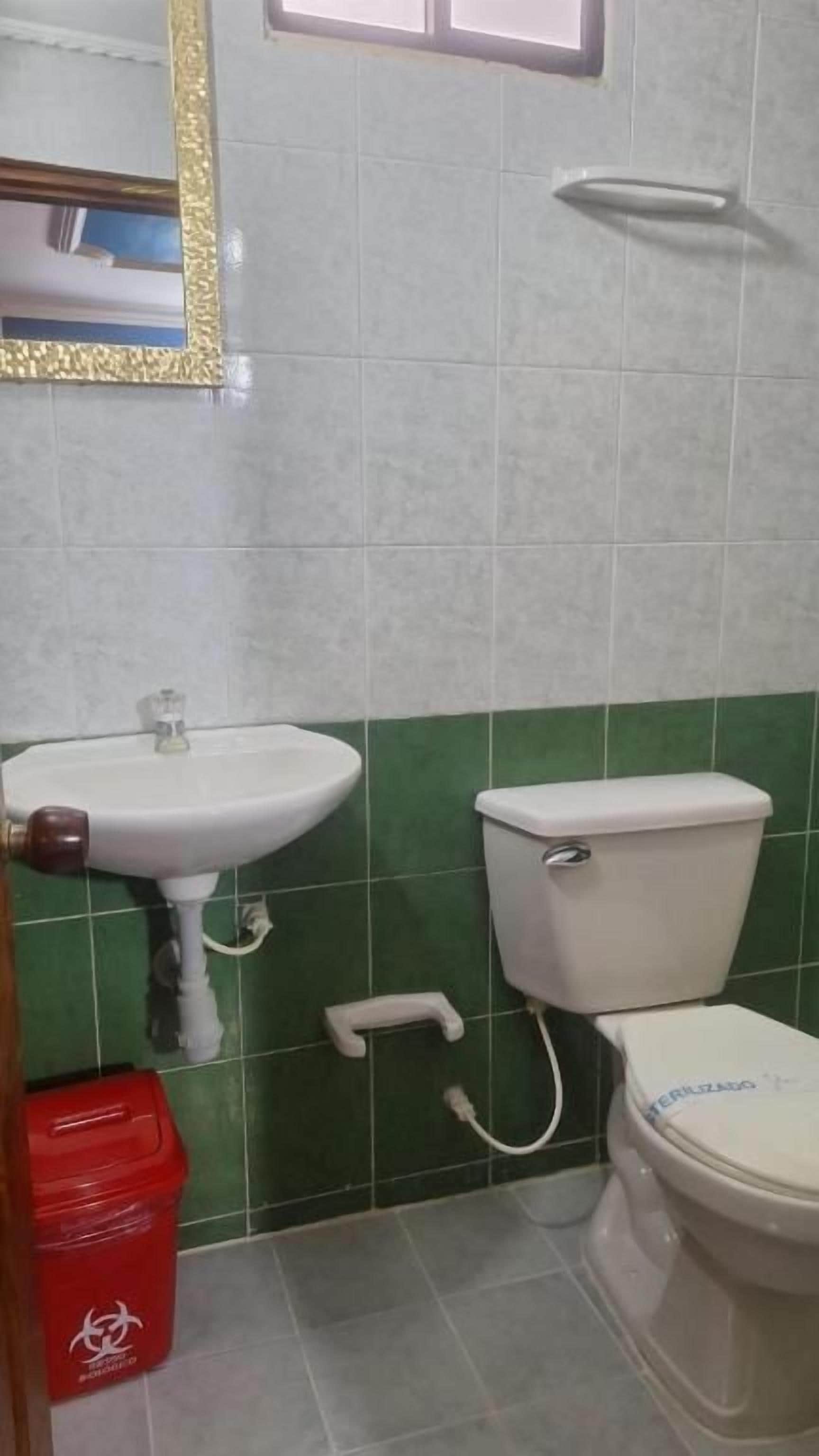 Un bany amb un vàter blanc, un lavabo i parets amb rajoles verdes.