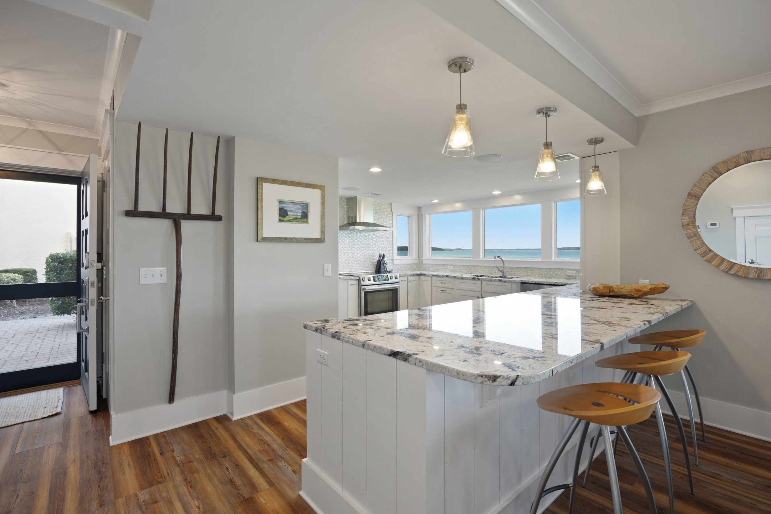 A modern kitchen with a large island, bar stools, and a view of the sea through large windows.