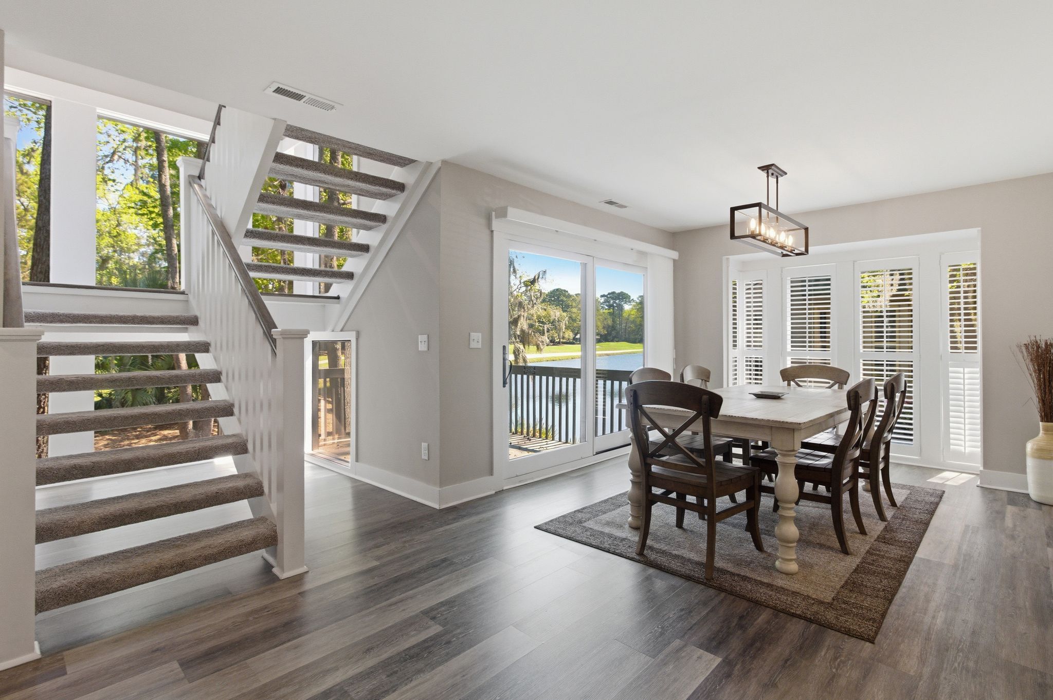 A dining area with a wooden table and chairs, a staircase, and a view of the outdoors.
