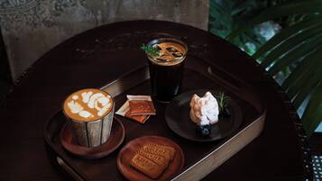 A tray with a coffee cup, a glass of dark beverage, a small figurine, and a cookie on a wooden table.