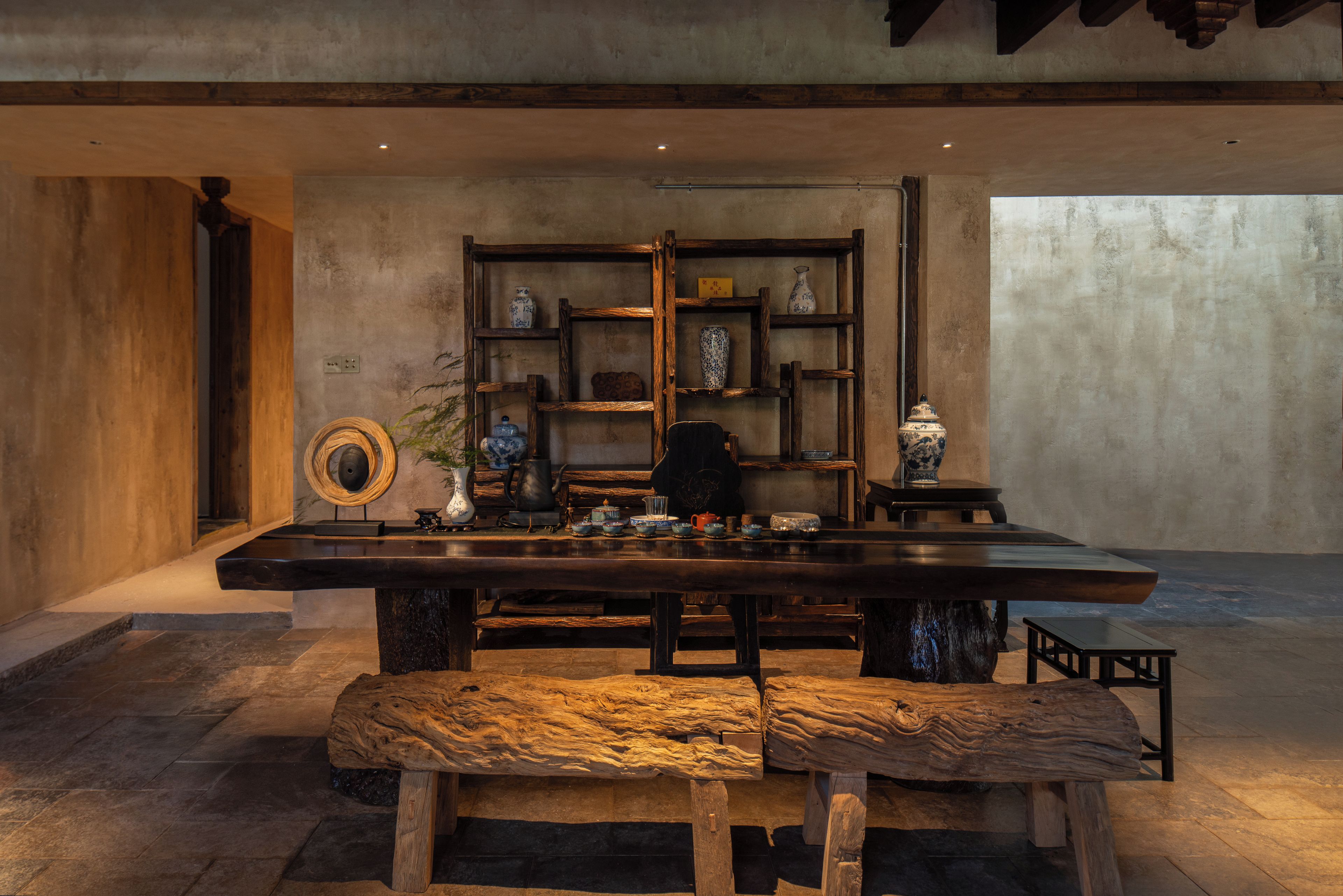 A rustic interior with a wooden table, benches, and shelves with various items.