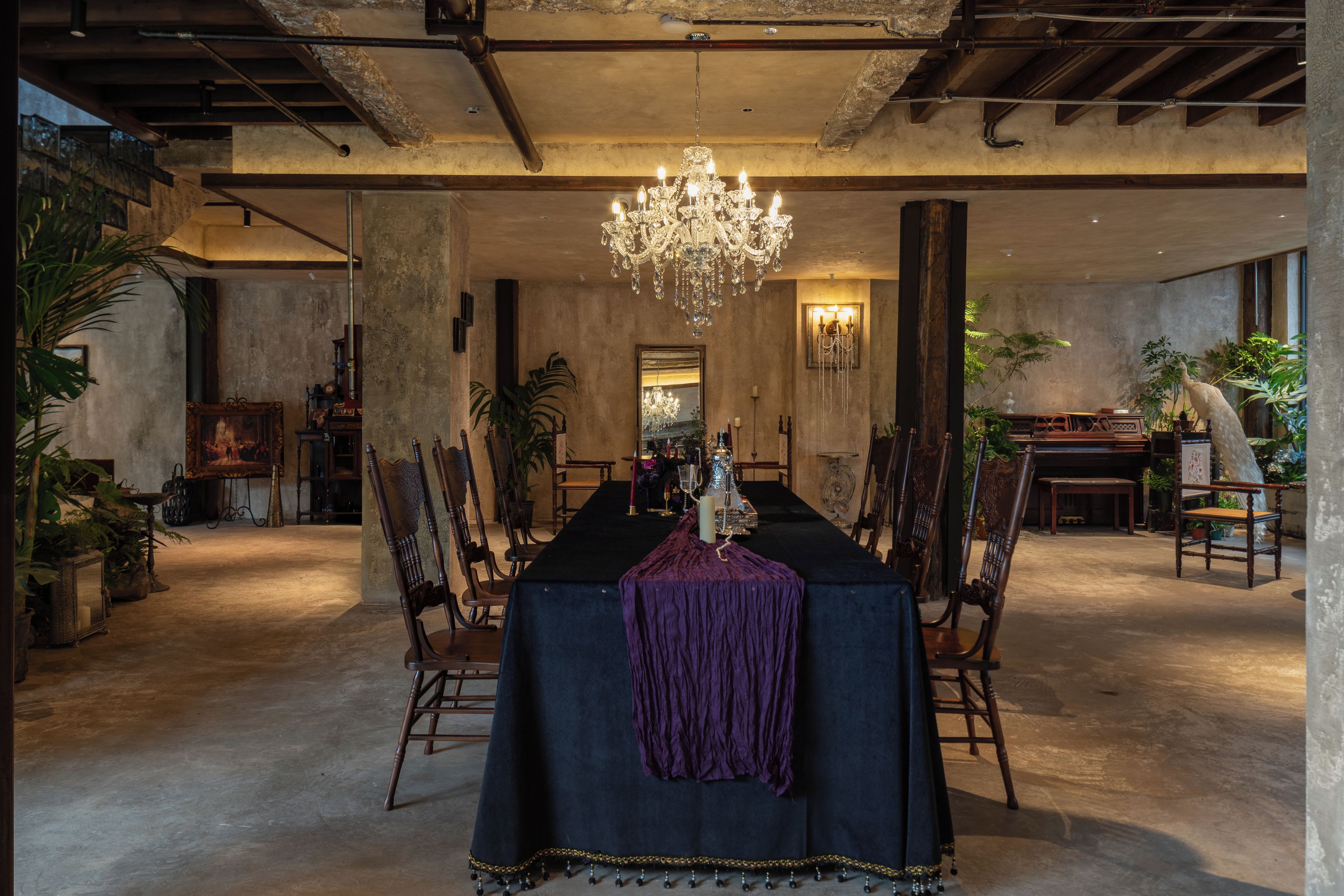 Een eethoek met een lange tafel, stoelen, een kroonluchter en diverse decoratieve objecten.