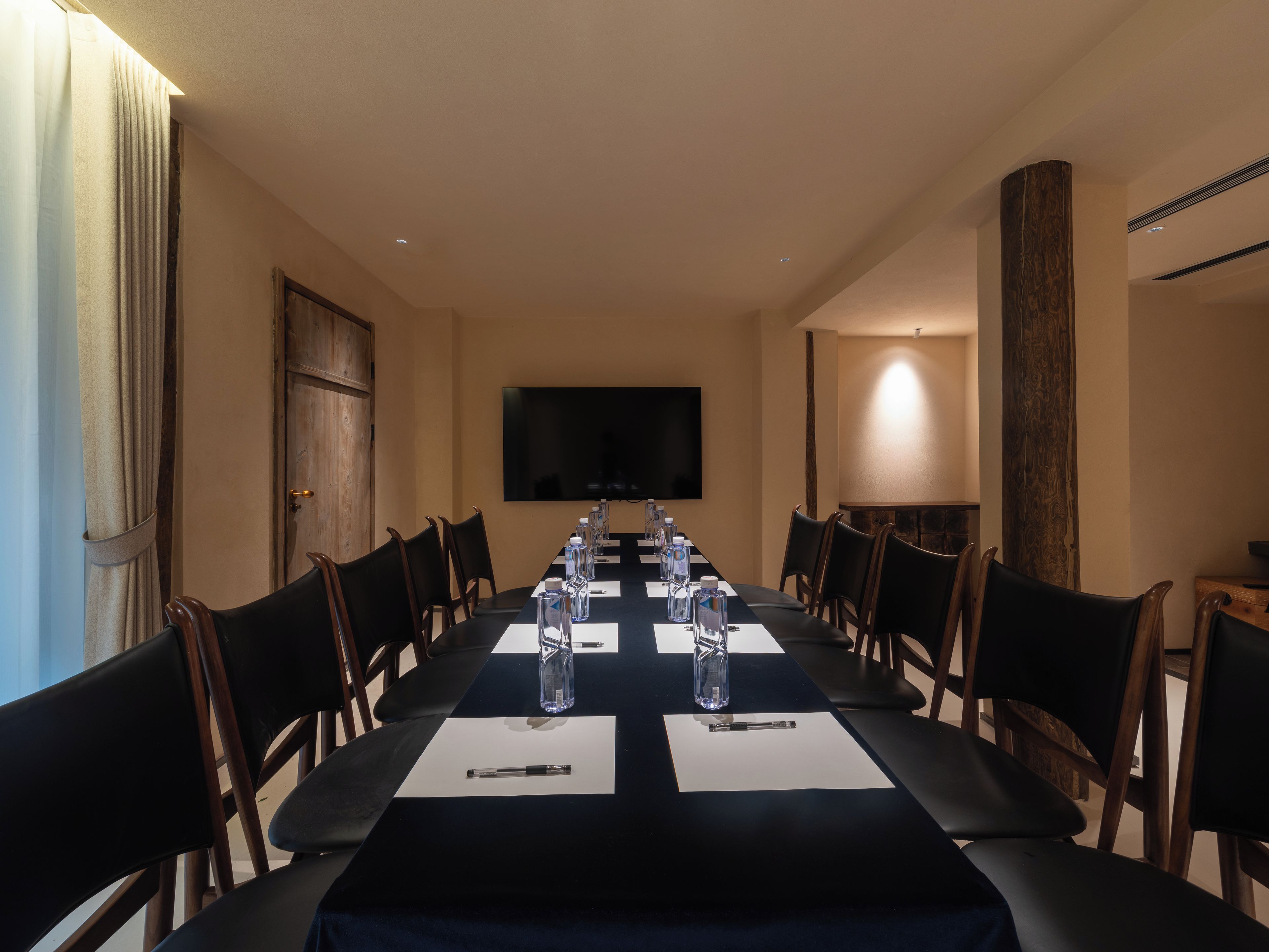 Un salón de conferencias con una larga mesa, sillas, botellas de agua y un televisor de pantalla plana.