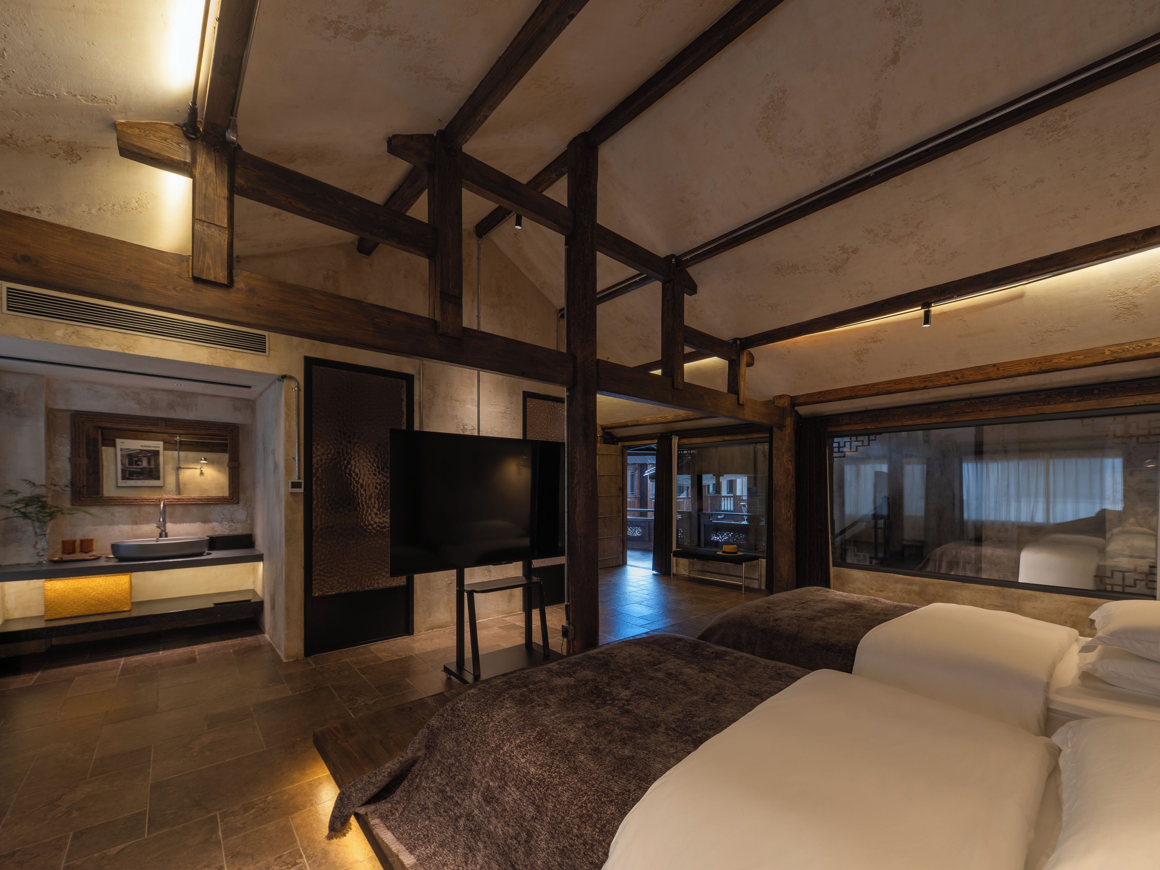 A hotel room with a large bed, a TV, a bathroom with a sink, and a view of the outside.