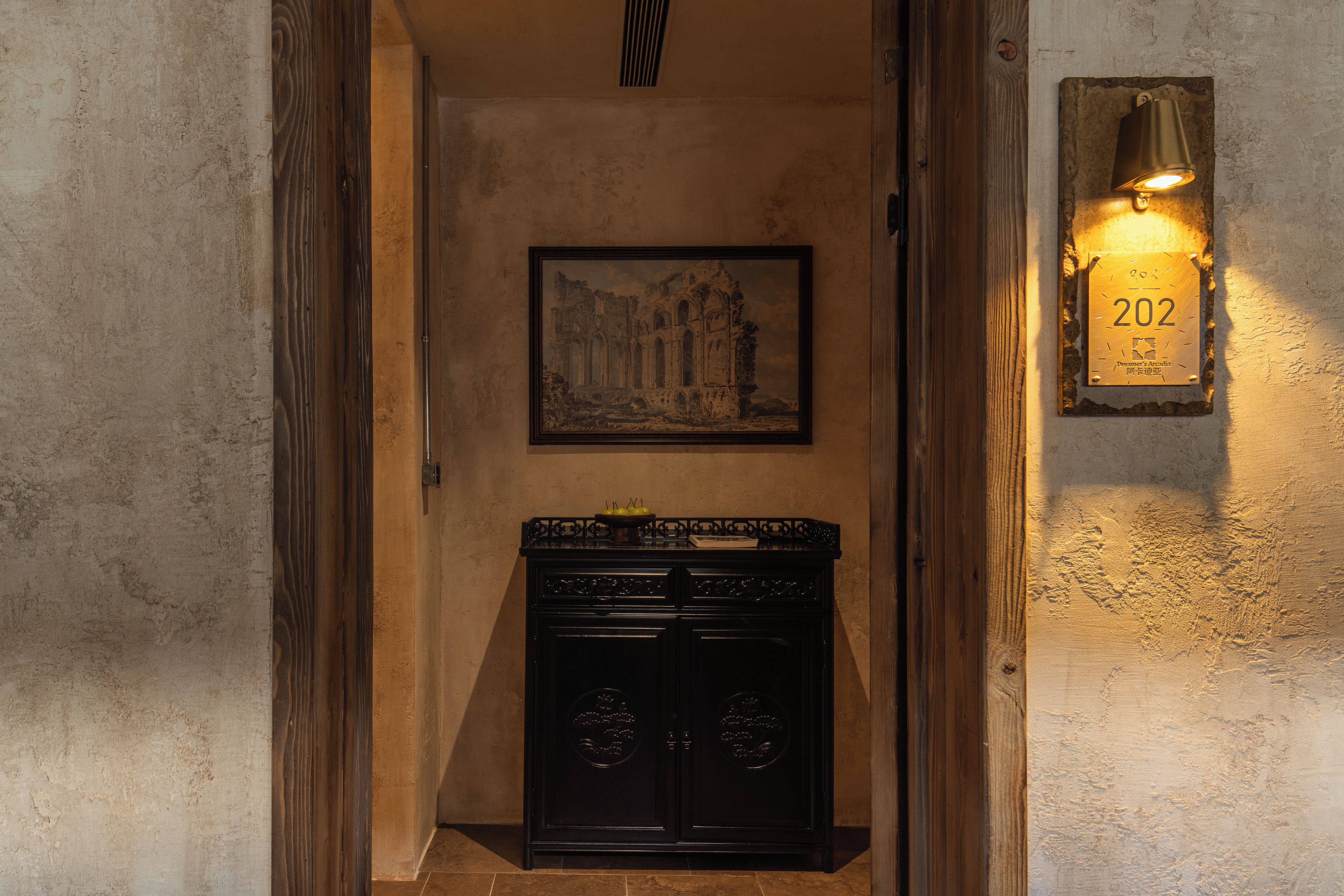 Un pasillo con un cuadro histórico enmarco, un mueble negro y una lámpara de pared con una placa de número.