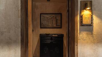 Un pasillo con un cuadro histórico enmarco, un mueble negro y una lámpara de pared con una placa de número.