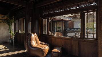 Ein Zimmer mit Ledersessel, kleinem Hocker und großem Fenster mit traditionellem Gittermuster.