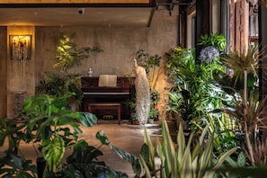Habitació amb un piano, una escultura de bust i diverses plantes.
