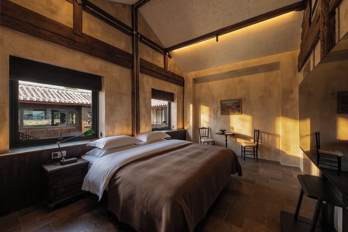 A bedroom with a large bed, wooden headboard, bedside tables, a desk, and a chair.