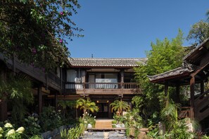 A traditional building with a wooden balcony, surrounded by lush greenery and a small water feature.