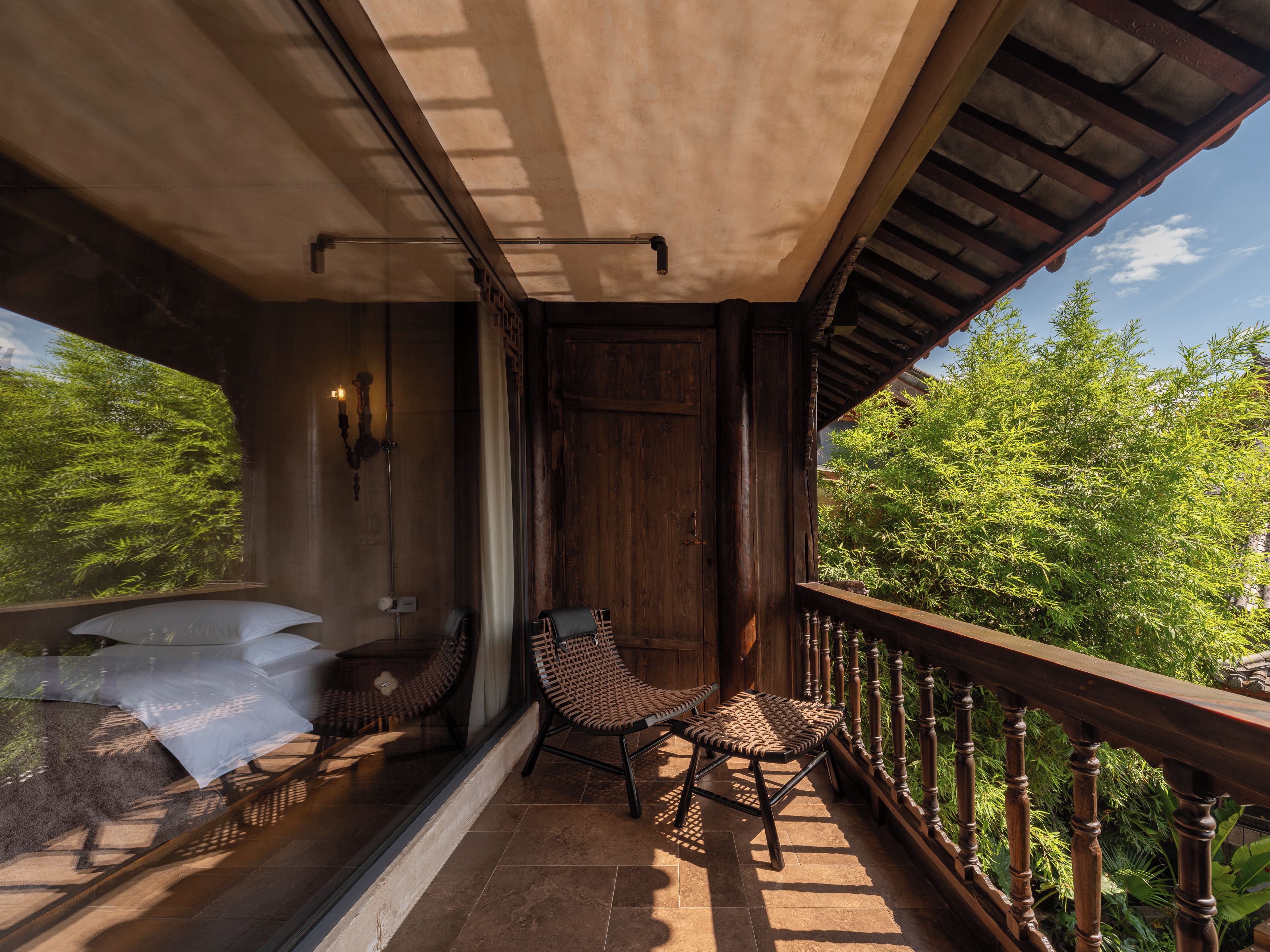 A balcony with a wooden railing, a wicker chair, a cushioned bench, and a view of greenery.