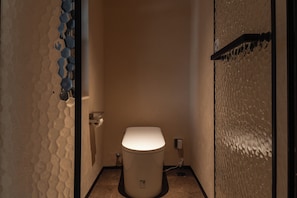 Un baño pequeño y estrecho con inodoro blanco, un perchero y un dispensador de papel higiénico en la pared.