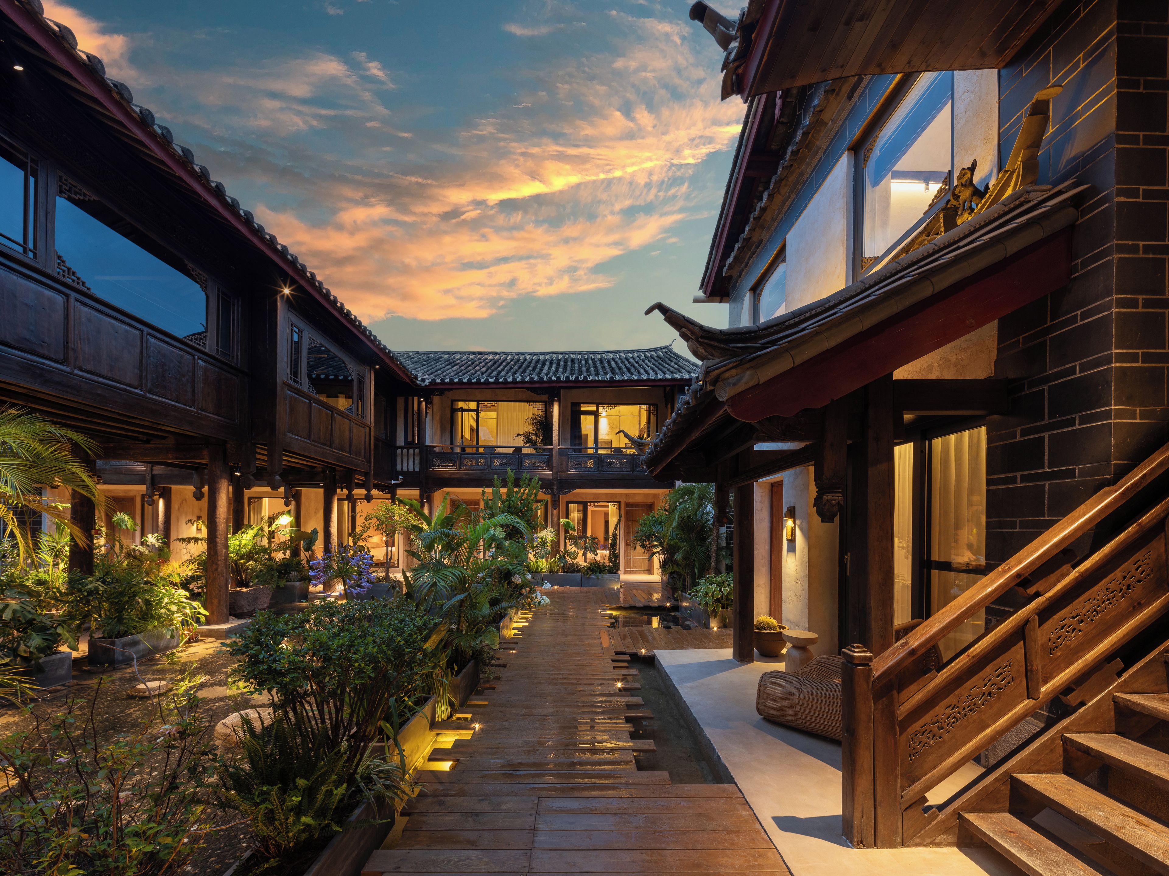 Une cour traditionnelle dotée d’une architecture en bois, d’un chemin central et d’une végétation luxuriante tout autour.