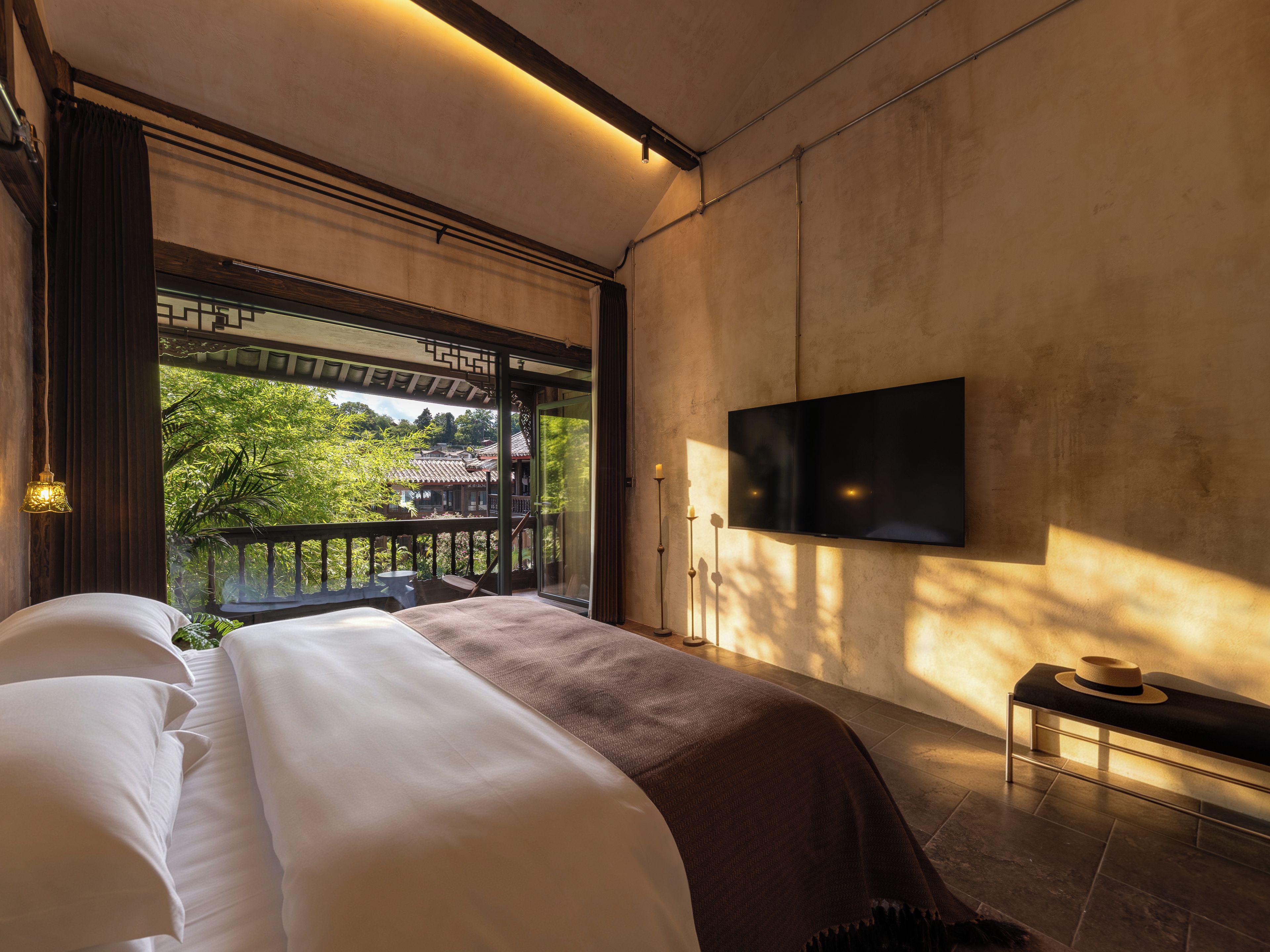 Une chambre dotée d’un grand lit, d’un téléviseur fixé au mur et d’un balcon offrant une vue sur la verdure.