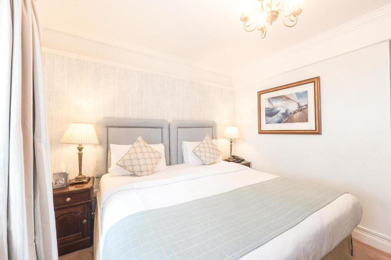 A hotel room with a large bed, two bedside tables, a nightstand, a chandelier, and a framed picture on the wall.