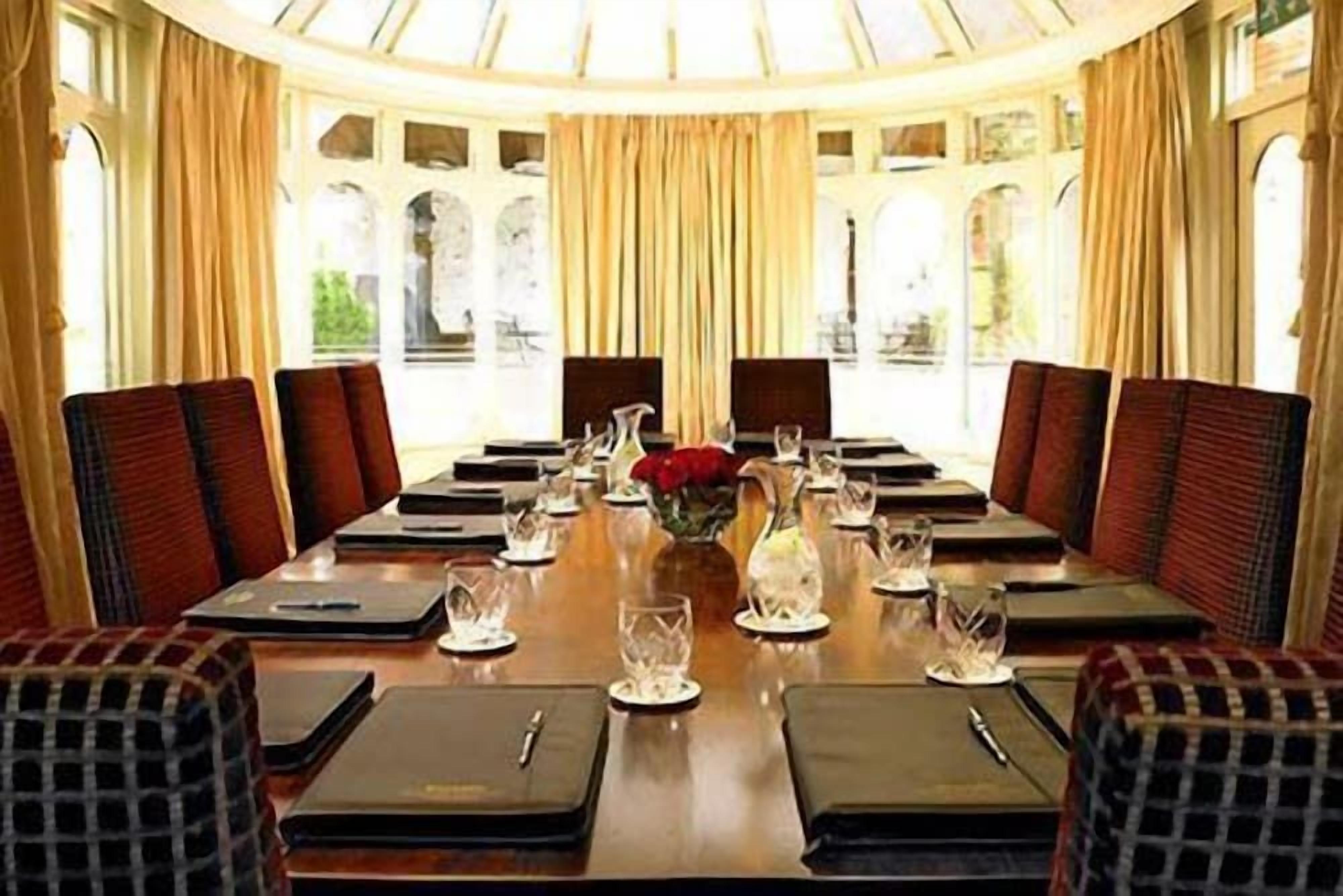 A conference room with a long table, chairs, and a vase with red flowers.