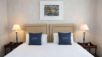 Una habitación de hotel con una cama grande, dos mesitas de noche con lámparas y un cuadro en la pared.