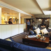 A hotel lobby with a reception desk, a stone fireplace, a sofa with cushions, and a coffee table with a book and a glass.