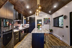 A modern kitchen with dark cabinetry, a granite countertop, and a central island. - Haven Haus Properties (Eagle River)