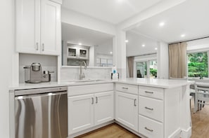 A modern kitchen with white cabinetry, a stainless steel dishwasher, and a view of the outdoors through a sliding glass door. - 2307 Heritage Villas at The Sea Pines Resort (Hilton Head Island)