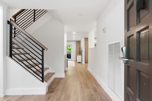 Ein modernes Interieur mit einer Holztreppe, einem Flur, der zu einer Tür führt, und Blick auf einen Balkon.