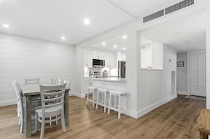 A modern kitchen with white cabinetry, a central island, and a dining area with a wooden table and chairs. - 2307 Heritage Villas at The Sea Pines Resort (Hilton Head Island)