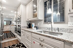 A modern kitchen with white cabinetry, granite countertops, stainless steel appliances, and a large window with decorative glass. - 1030 Caravel Court at The Sea Pines Resort (Hilton Head Island)
