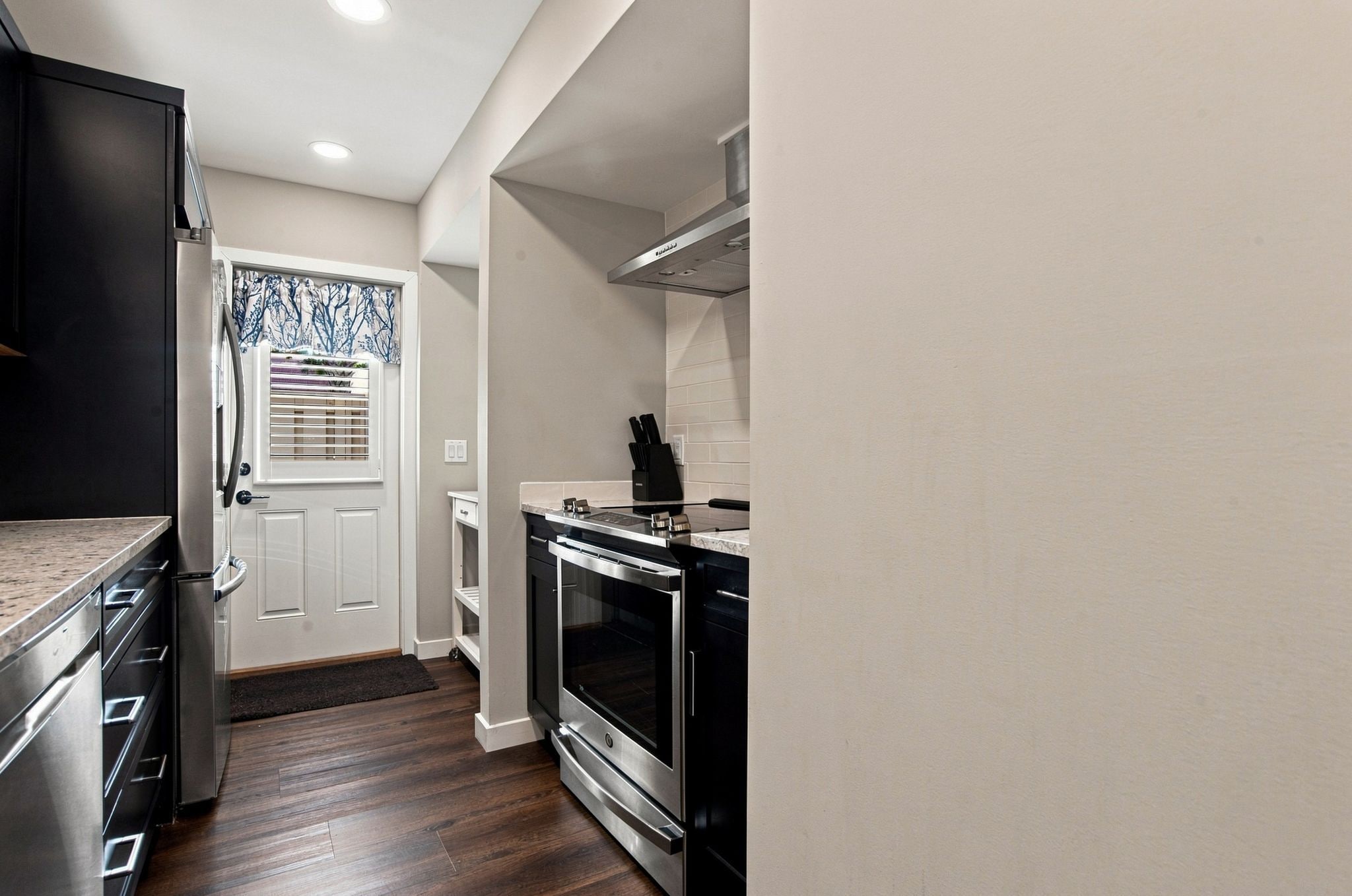 Una cocina compacta con horno integrado, un refrigerador y una ventana con persianas.