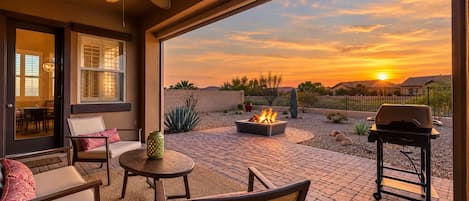 An outdoor patio with a fire pit, seating, and a view of the sunset.