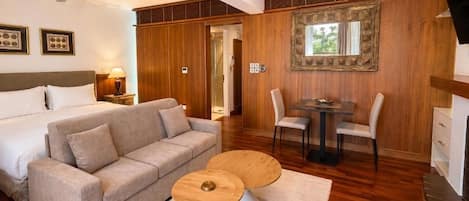 A hotel room with a bed, a sofa, a dining table with chairs, a ceiling fan, and a large mirror on the wall.