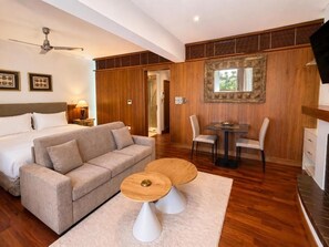 A hotel room with a bed, a sofa, a dining table with chairs, a ceiling fan, and a large mirror on the wall. - Ithaki Beach Apartment by TrulyCyprus (Lemesos)