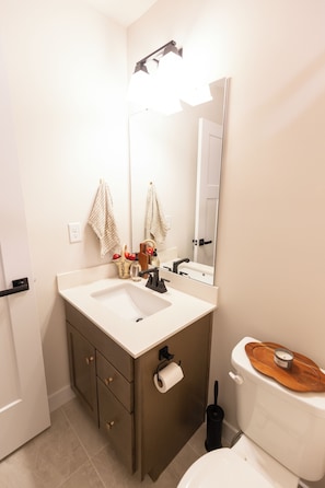 Ein Badezimmer mit einem weißen Waschbecken, einem Spiegel, einer Toilette und einer Holztablett auf dem Toilettendeckel.